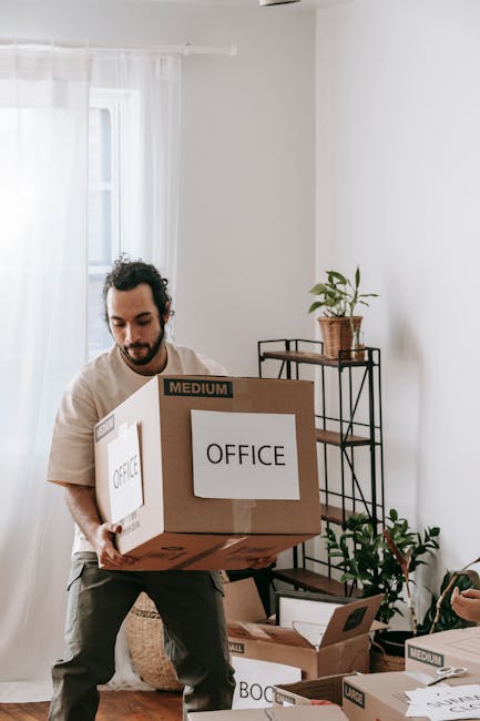 Inside a storage or office space, a wooden desk is positioned in the foreground with a closed brown paper parcel, a cup of coffee, a clipboard with papers, and writing utensils arranged on its surface